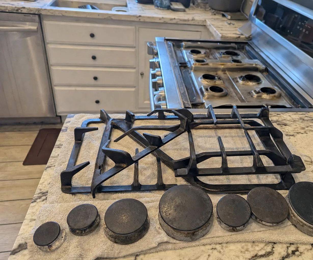 A stainless rangetop with every grate and cap lifted off and arranged on the island in front of it, burner heads open to view