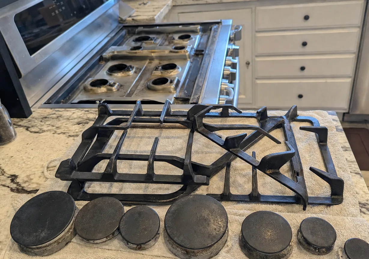 A stainless rangetop with the grates set aside, the sealed burner heads and their ports open to the light
